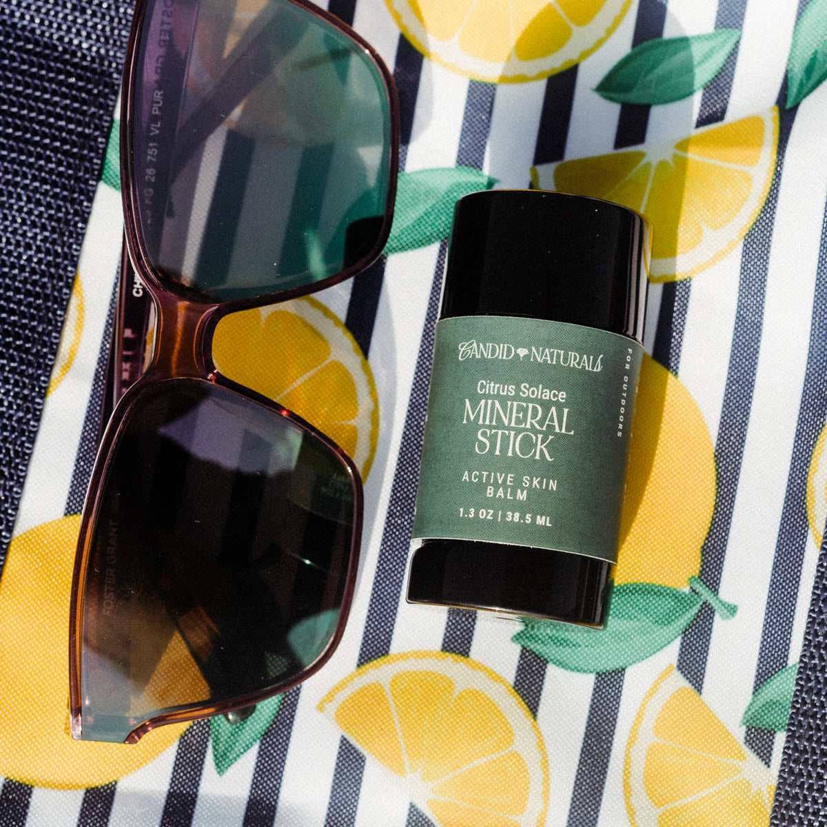 Close-up of Candid Naturals Citrus Solace Mineral Stick on a lemon-print bag with sunglasses
