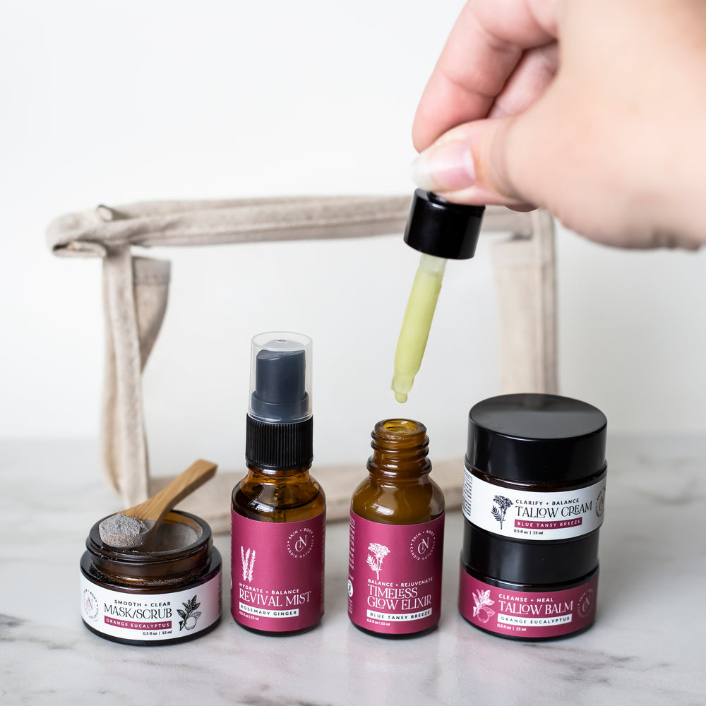 Hand holding a dropper over a collection of skincare products on a marble surface.