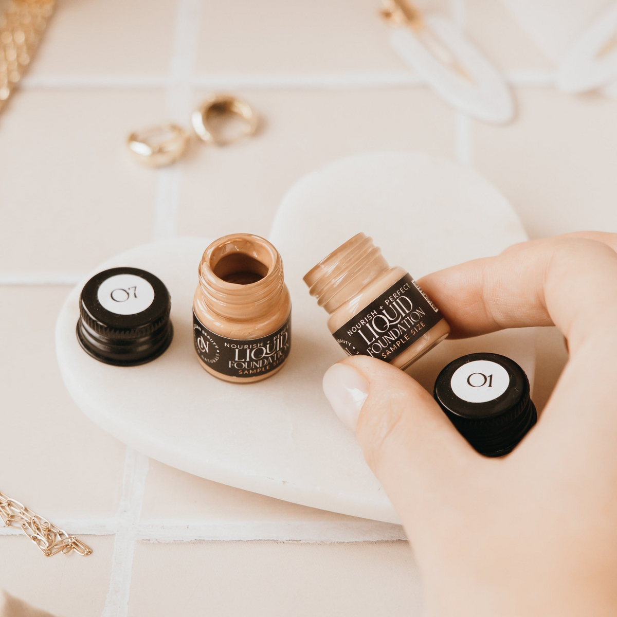 Hand holding an open Candid Naturals foundation sample jar from the Find Your Shade Sample Pack