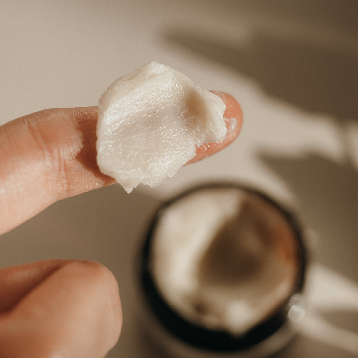 Fingertip holding a dab of Candid Naturals Herbal-Infused Tallow Cream next to the open jar