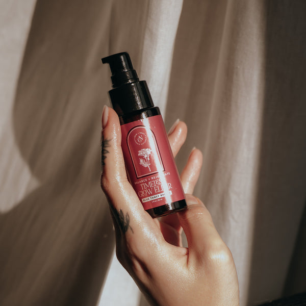 Hand holding a red skincare bottle with pump dispenser against a neutral background